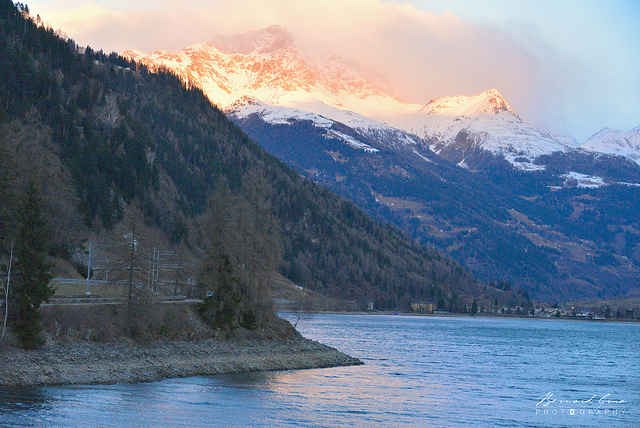 Miralago: le train longe le lac de Poschiavo (965m) encore dans l’ombre alors que les sommets sont atteints par les rayons du soleil – 08:09 © Bernard Grua